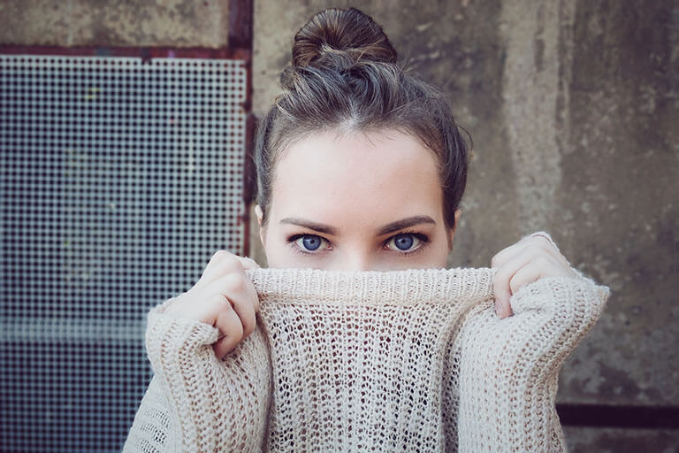 Dies Bild zeigt eine Junge Frau, die sich ihren Pullover über das Gesicht zieht. Ihre Augen sind dennoch zu erkennen. Erkennen und überwinden Sie ihre Lebenskrisen.